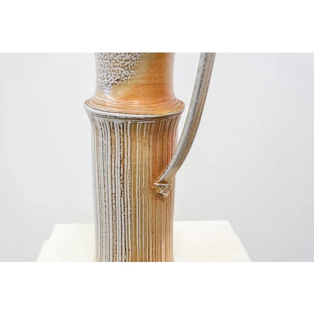 Glazed ceramic jug made of tubular body with a single handle. Textured relief decoration on the body consisting of grooves...