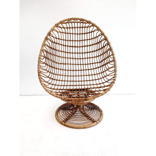 This vintage rattan lounge chair features a dramatic high-backed, egg-shaped silhouette with an open woven construction....