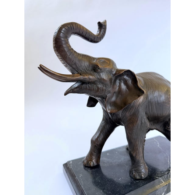 This bronze sculpture captures the majesty of a bull elephant in mid-stride, its trunk raised high in a classic gesture of...