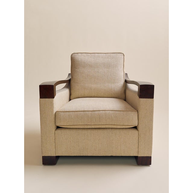 This armchair pairs a tailored beige upholstered body with sculptural walnut arms and a matching walnut base, creating a...
