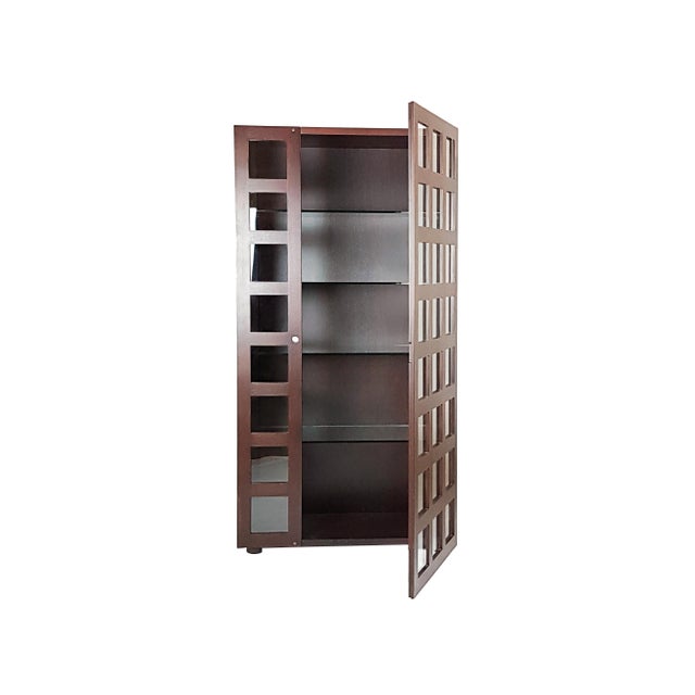 This bookcase or vitrine cabinet is made from a wooden structure with a grid design front side. It features a unique door...