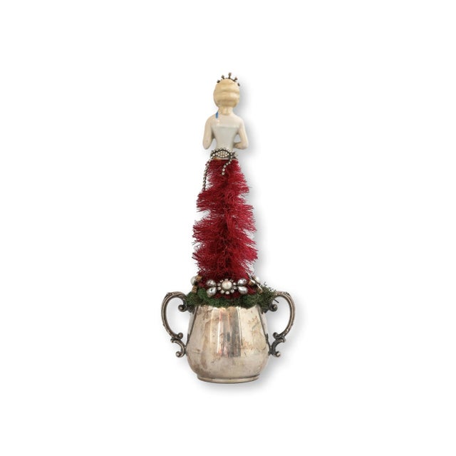 This dazzling holiday tree is giving full Queen energy. An antique porcelain brush doll crowns the top, reimagined as a...