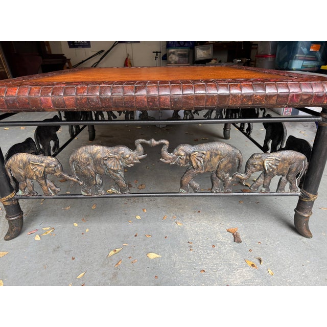 Maitland-Smith figural coffee table featuring a warm tan hand-tooled leather top with a woven leather border, set on a...