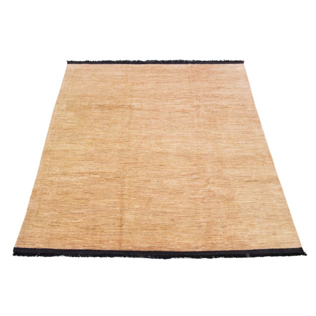This handcrafted wool rug, designed in the Gabbeh style, features a solid design highlighted by black fringes and a beige...