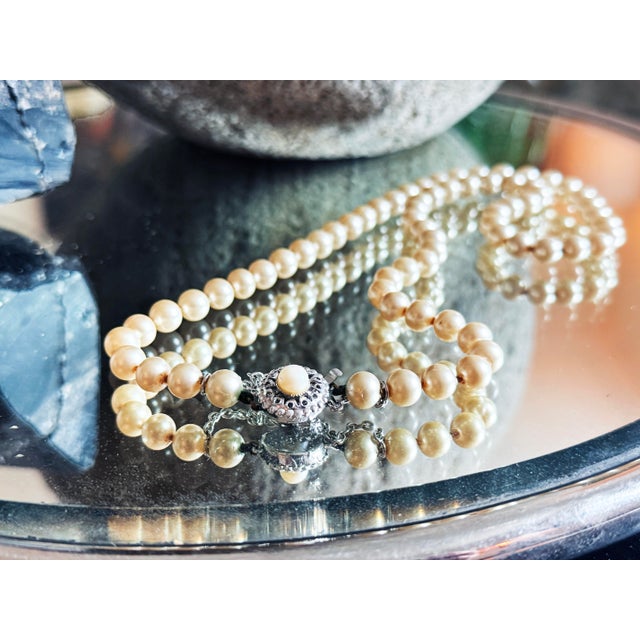 Vintage Mid Century single strand necklace featuring warm ivory to cream glass faux pearls and an ornate silvertone...