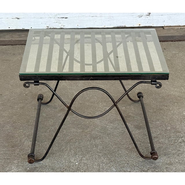 This small wrought iron table rests on a folding-style X-frame of looped and scrolled rods. A slatted iron top with a...