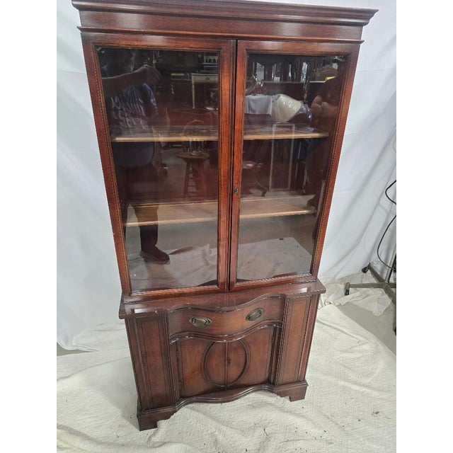 Elegant vintage mahogany curio cabinet featuring a refined silhouette with a serpentine front base, glass-paneled upper...