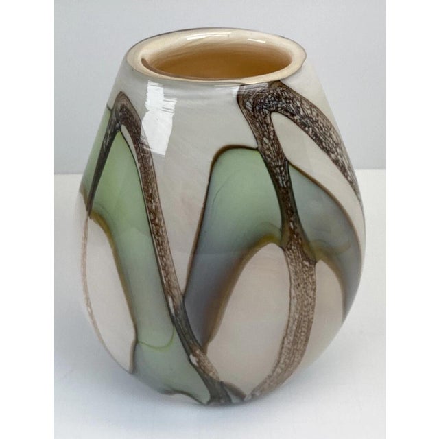 A distinctive hand-blown art glass vase featuring a sophisticated blend of cream, green, and brown tones in a modern...