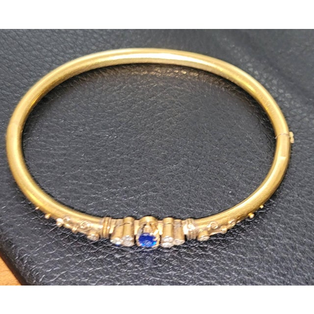 Subtle elegance in this circa 1880s solid 14k gold tested bangle with center sapphire and 8 small diamond surrounds. Clasp...