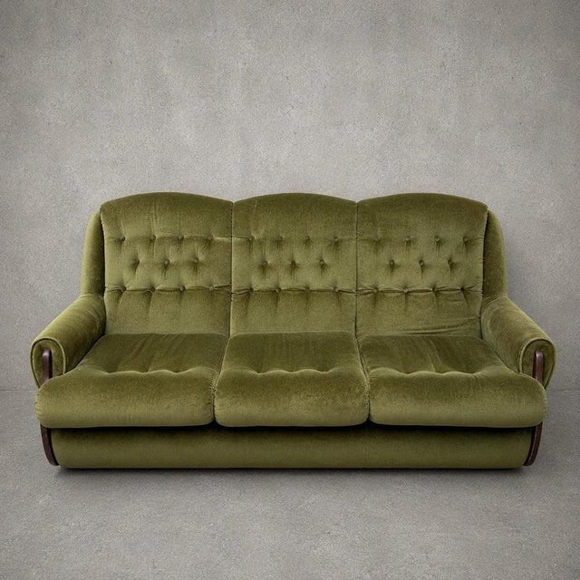 A striking mid century three-seater sofa upholstered in its original olive green velvet, offering generous proportions,...