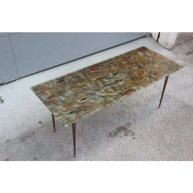 This is a Cristal Art 1950s table, with hammered metal feet, and glass plate with decorations typical from the period....
