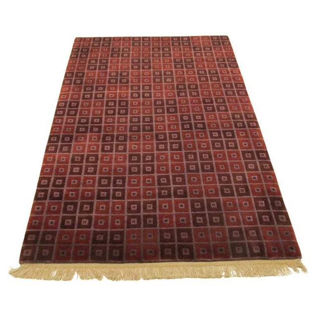 This hand knotted pile rug features a primary red and rust color palette suitable for a variety of interior settings....