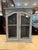 A charming vintage wooden wall cabinet with glass-paneled doors and a beautifully distressed painted finish. The weathered...