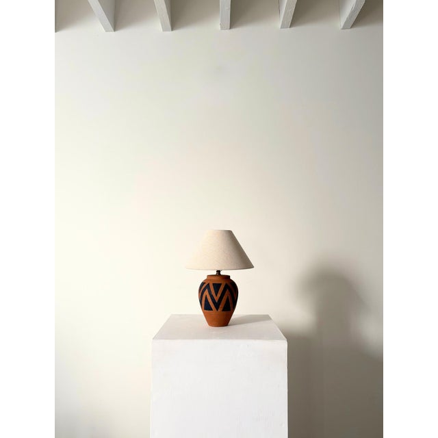 A vintage terracotta table lamp, hand painted with geometric chevron motifs which wrap around the entire lamp base with...