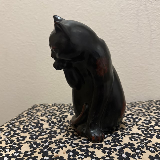 This charming vintage figurine is made of ceramic and features a sleek black cat in a seated, grooming pose. The piece has...