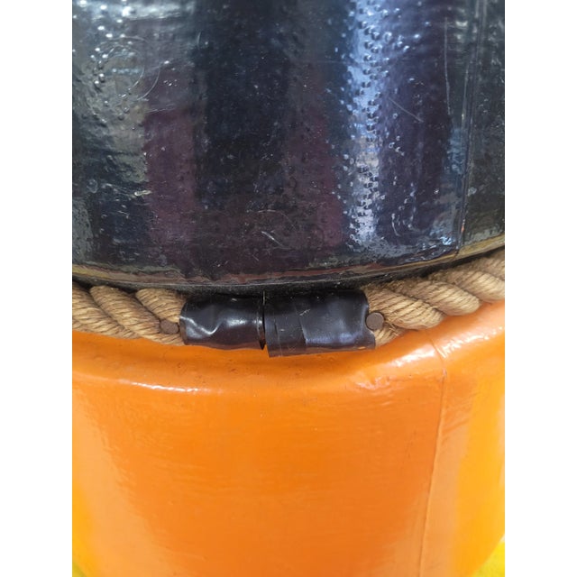A bold and authentic mid-century commercial fishing buoy, painted in signal orange and black with its original rope seam...