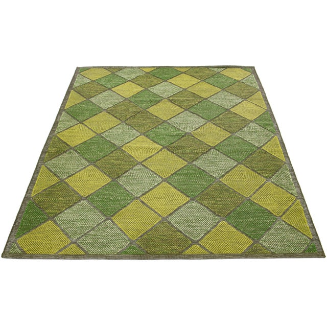 This flatweave rug features a modern Swedish design with a green base. Beige, light green and yellow geometric patterns...