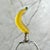 Lamp finial crafted from a glass banana mounted on shiny chrome hardware sized to fit a standard-size lamp with a 1/4" stem.