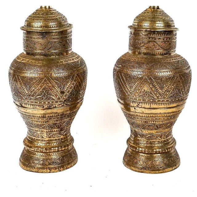 A pair of Anglo-Indian style brass table lamps featuring richly embossed urn form bodies with intricate geometric,...