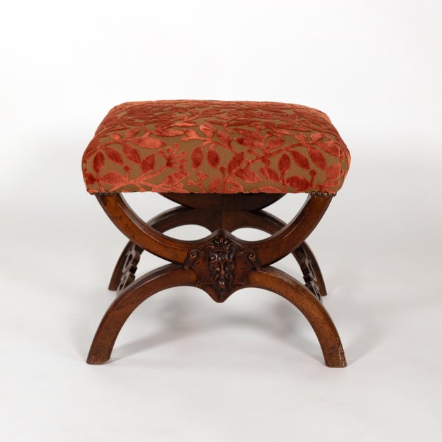 Carved walnut stool of curule form, the opposing X-frames centered to each end by fairly dignified and naturalistically...
