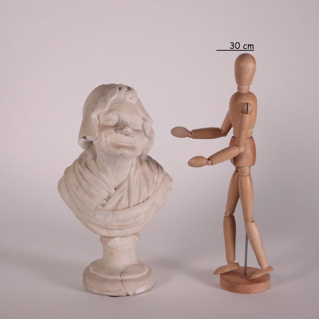 Small marble bust placed on a circular base, depicting an elderly woman with typical physiognomic features; her shoulders...