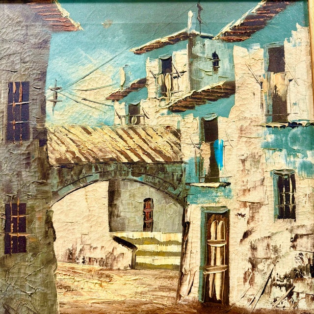A large oil painting in a giltwood frame depicting a quiet street in an old Spanish town. The narrow road is lined with...
