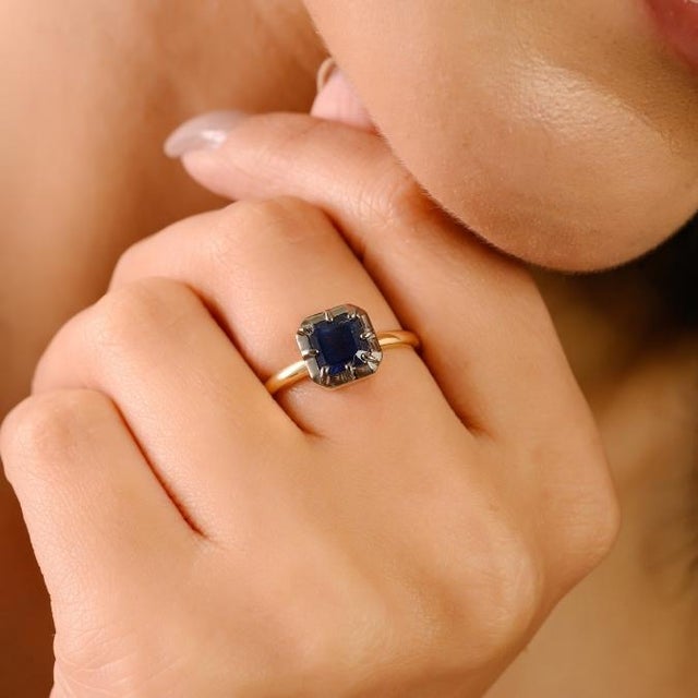 This elegant solitaire ring features a 1.33 carat Asscher-cut blue sapphire set in a sleek 18K yellow gold band, featuring...