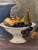 A vintage oil painting on Masonite depicting a young boy seated beside a still life arrangement of fruit and a dark...