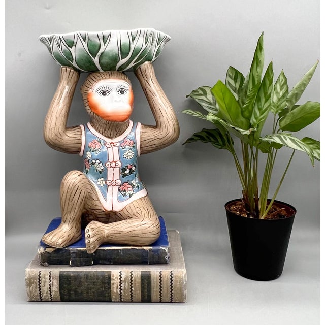 Delightful ceramic monkey seated with raised arms supporting a green-and-white bok choy–style bowl overhead, a design also...