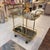 A beautiful vintage brass rolling bar cart in the style of D.I.A. The bottom shelf has mirrored smoked glass with a built...