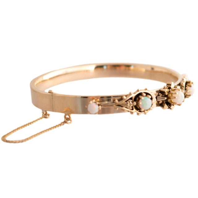 This hinged bracelet features a 14k yellow gold design with ornate detailing. The bracelet showcases five opals set in...