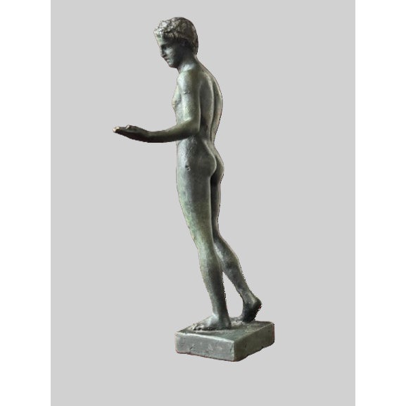 A classical bronze sculpture depicting an idealized nude male figure rendered in a graceful contrapposto stance, with...