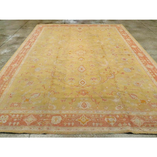 An antique Turkish Oushak room size carpet. Big leaves angularly bend to nearly enclose small palmettes while others reach...