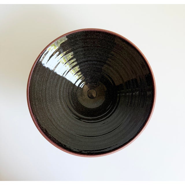 A striking hand-thrown studio pottery bowl featuring a red clay body and dark gray glazed interior, dramatic tapered...