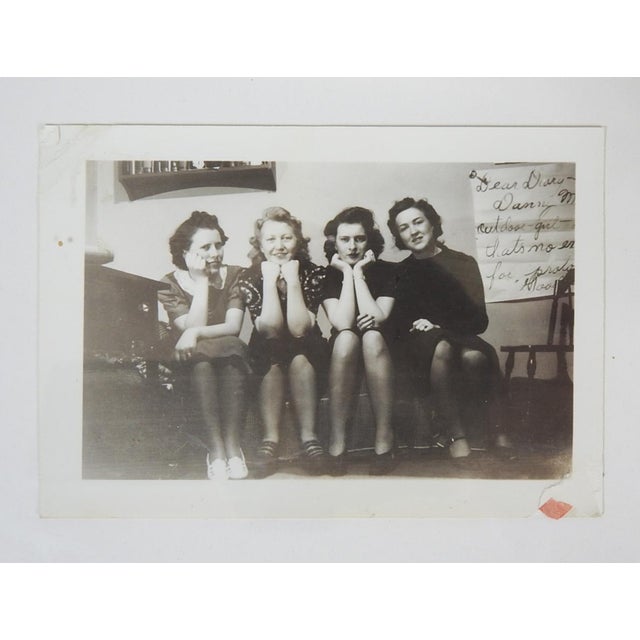 1950's vernacular snapshot photograph of a group of women sitting on a sofa. On the wall behind them is a large image of a...
