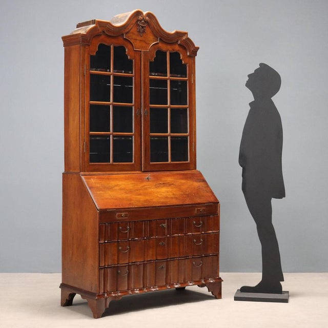 Walnut trumeau. Stand with a pair of glass doors, a carved scrollwork pediment with a central floral composition, a drop-...