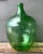 This vintage green glass demijohn bottle is a striking example of mid-20th-century utilitarian glassware, prized today for...