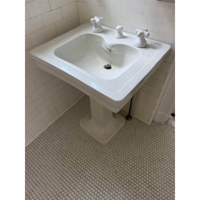 A beautifully intact antique pedestal sink in classic all-white porcelain, likely dating from the early-to-mid 20th...