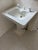 A beautifully intact antique pedestal sink in classic all-white porcelain, likely dating from the early-to-mid 20th...