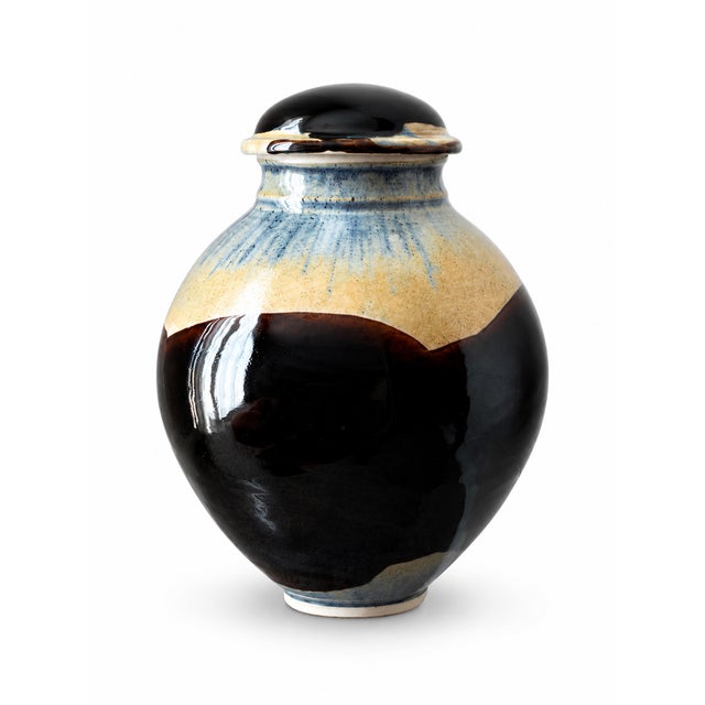 A sculptural pottery covered jar featuring a rounded body, narrowed neck, domed lid, and defined foot ring. Sweeping...