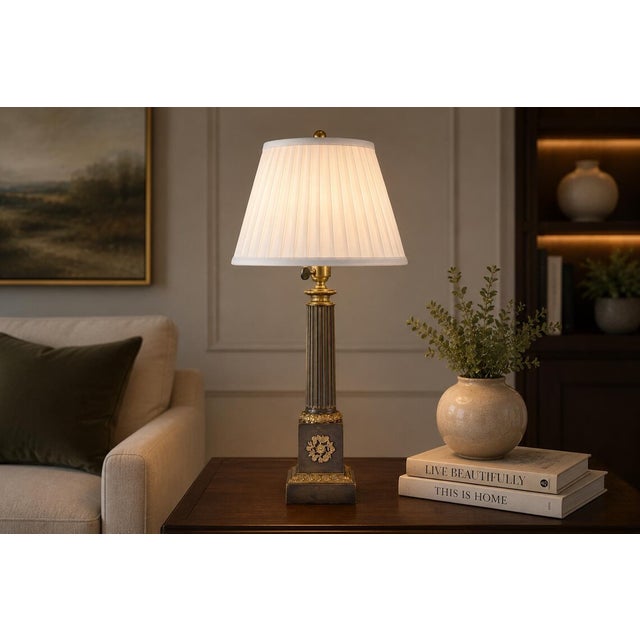 A stately antique bronze table lamp in the Neoclassical column form, drawing directly from the Louis XVI decorative...