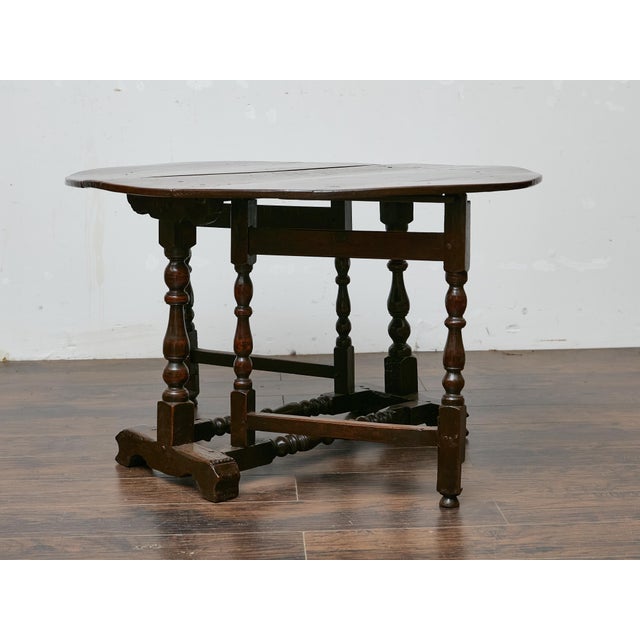 An English oak drop-leaf gateleg table from the 19th century, showcasing a rich, dark finish and a practical design rooted...