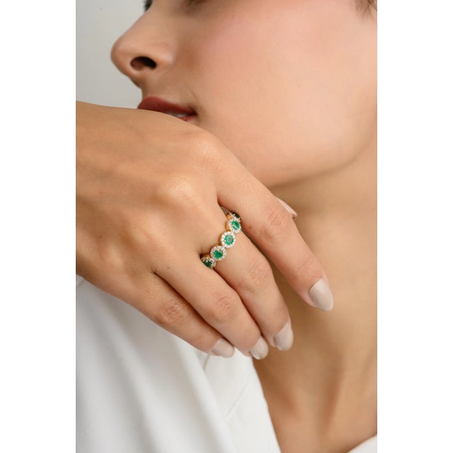 This elegant wedding band features five natural round-cut emeralds, each encircled by a dazzling halo of diamonds. The...