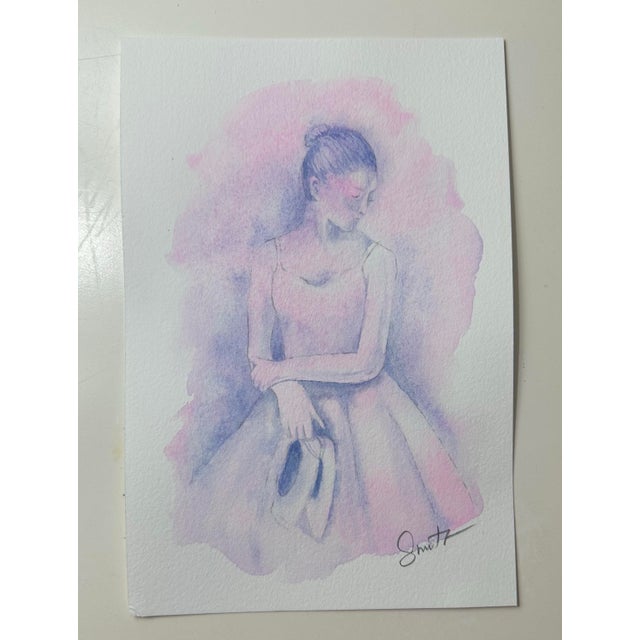 A delicate watercolor portrait of a young ballerina resting in a moment of reflection. Soft washes of blush pink and...