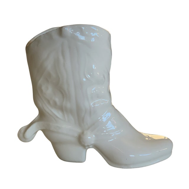 Vintage ceramic vase crafted in the form of a classic Western cowboy boot, finished in a glossy ivory-white glaze with...