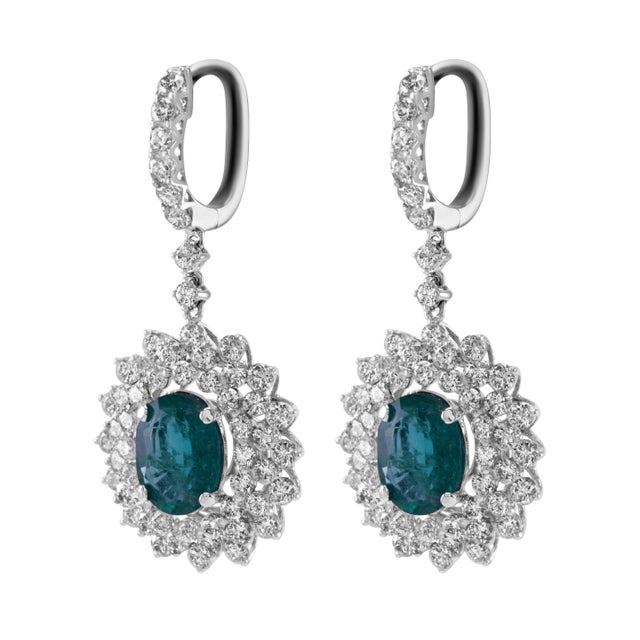 Beautiful natural oval emerald drop earrings with a diamond halo. 7.07 carats total gemstone weight. 2 oval emeralds, 3.19...