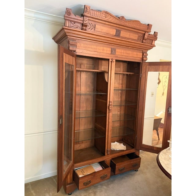 A monumental Victorian knockdown bookcase featuring two large glass doors, intricate wood carvings, engaged columns, and a...