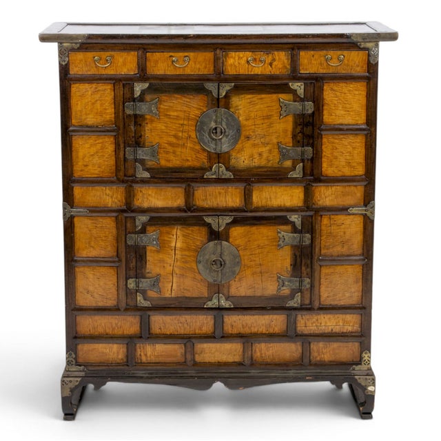 A striking Korean Bandaji-style cabinet, distinguished by richly figured wood panels, dramatic traditional brass hardware,...