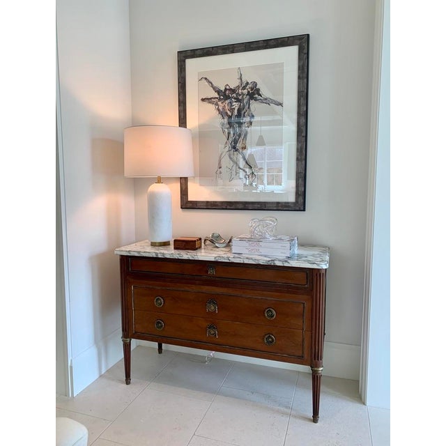 The Waterson lamp features a substantial white marble column base accented with antique brass detailing, creating a...