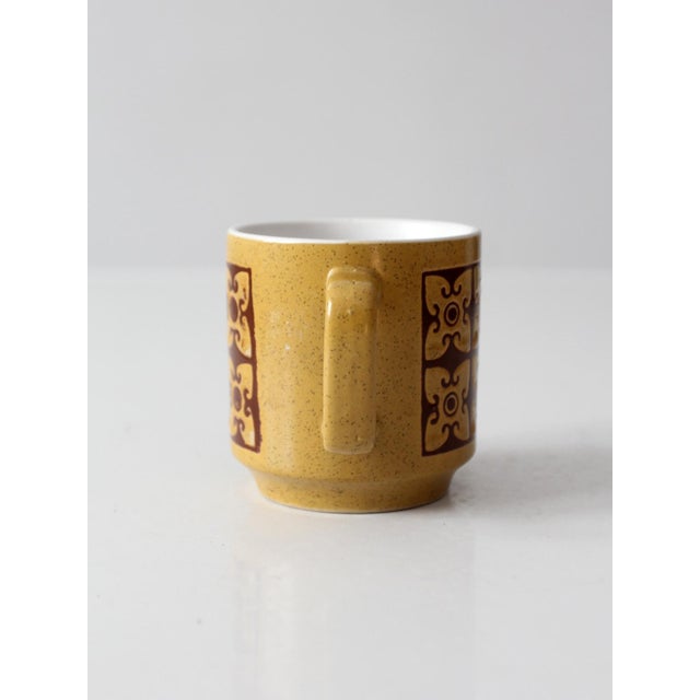 A vintage 1970s ceramic mug featuring a speckled mustard glaze with a bold chocolate brown geometric pattern wrapping the...